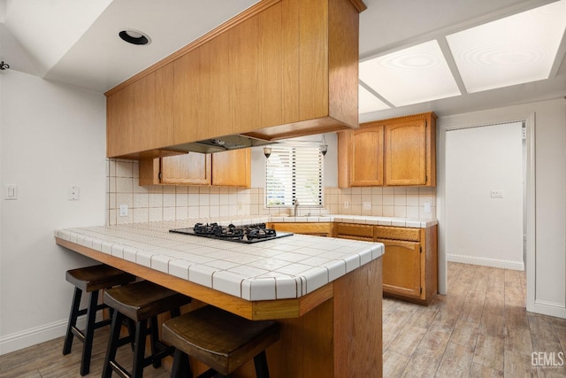 kitchen featuring tile counters, backsplash, black gas stovetop, and kitchen peninsula