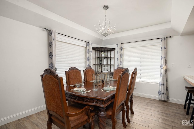 dining area with an inviting chandelier, a raised ceiling, and hardwood / wood-style floors