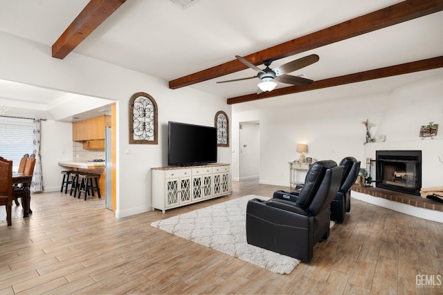 living room with beam ceiling, a brick fireplace, ceiling fan, and light hardwood / wood-style flooring