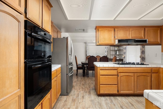 kitchen featuring tile counters, kitchen peninsula, light wood-type flooring, and black appliances