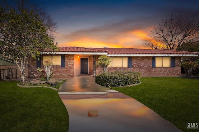 ranch-style home featuring a tile roof, brick siding, and a front lawn