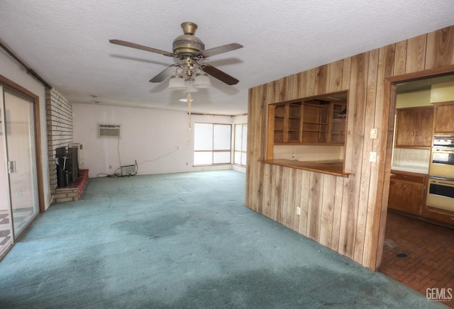 unfurnished living room featuring a textured ceiling, carpet floors, a fireplace, wooden walls, and ceiling fan