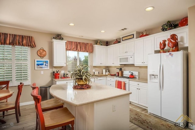 kitchen with white cabinets, a center island, white appliances, and hardwood / wood-style flooring