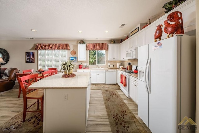 kitchen with a center island, white cabinets, white appliances, and light hardwood / wood-style flooring