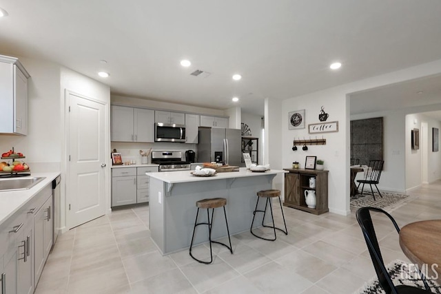 kitchen featuring gray cabinetry, a kitchen island with sink, sink, appliances with stainless steel finishes, and a kitchen bar