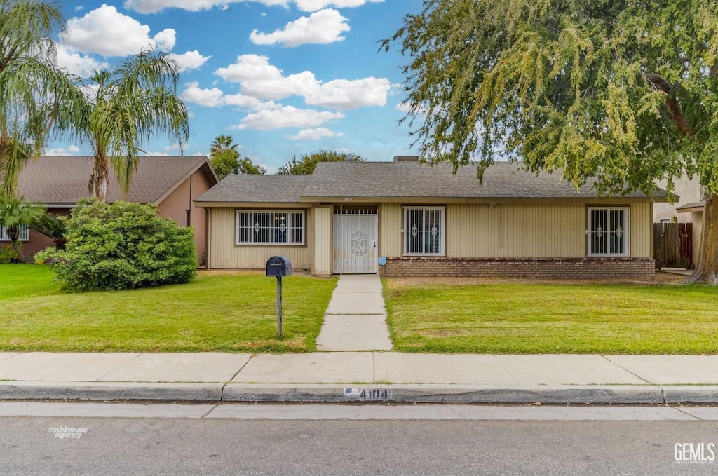 ranch-style home featuring brick siding, fence, and a front lawn