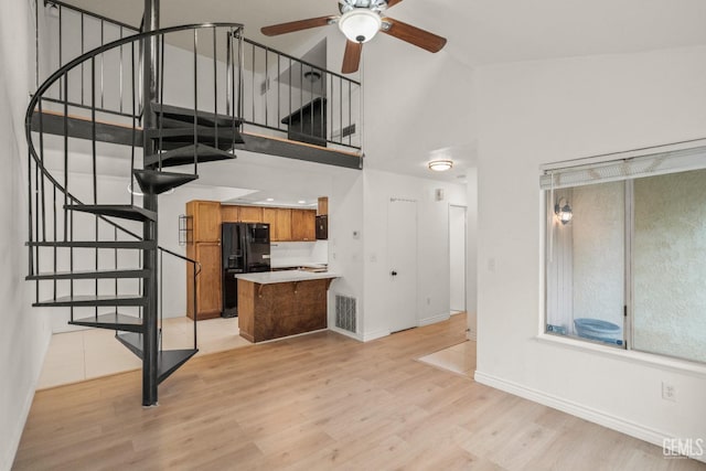 unfurnished living room with stairway, a high ceiling, light wood finished floors, visible vents, and a ceiling fan
