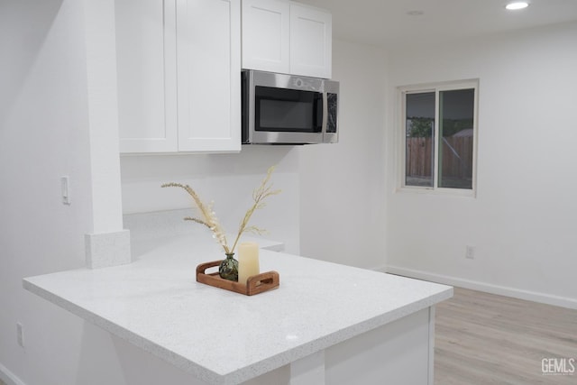 kitchen with stainless steel microwave, white cabinetry, recessed lighting, light wood-style floors, and baseboards