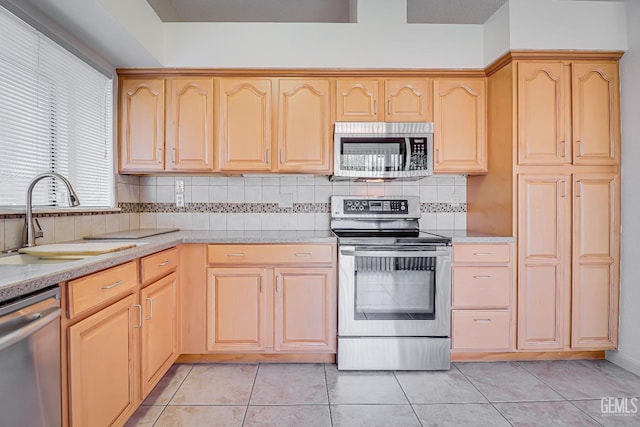 kitchen featuring light tile patterned floors, stainless steel appliances, tasteful backsplash, light brown cabinetry, and a sink