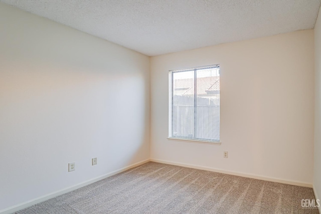 spare room with light colored carpet, a textured ceiling, and baseboards