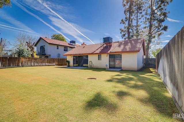 rear view of property with a tile roof, a yard, a fenced backyard, and stucco siding