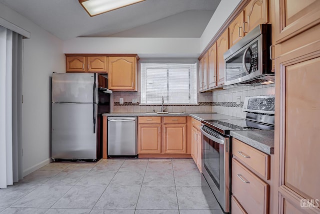 kitchen featuring tasteful backsplash, lofted ceiling, appliances with stainless steel finishes, a sink, and light tile patterned flooring