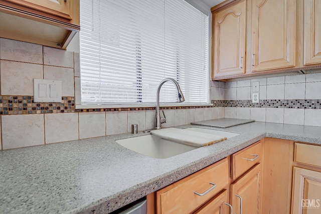 kitchen with light brown cabinets, light stone counters, backsplash, and a sink