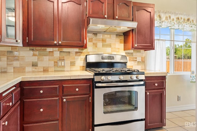 10801 Santa Clara St, Lamont, CA 93241 - kitchen featuring stainless steel gas stove, under cabinet range hood, reddish brown cabinets, light countertops, and decorative backsplash