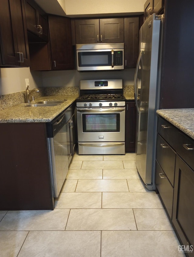 kitchen featuring sink, light tile patterned floors, dark brown cabinetry, stainless steel appliances, and light stone countertops