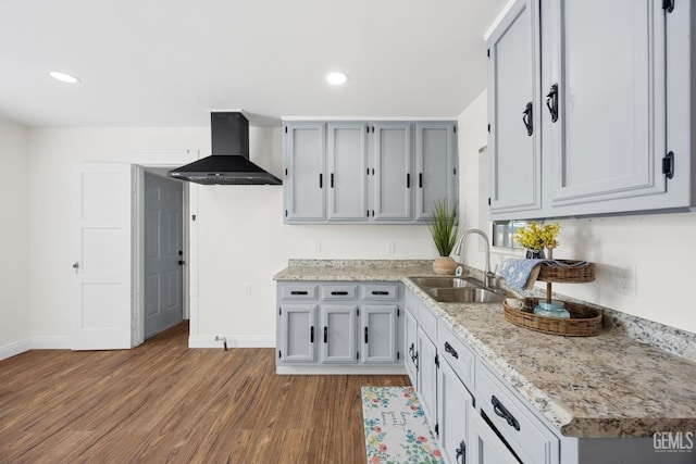 kitchen featuring wall chimney exhaust hood, baseboards, a sink, and wood finished floors