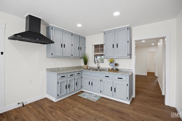 kitchen with wall chimney range hood, dark wood-type flooring, a sink, and recessed lighting