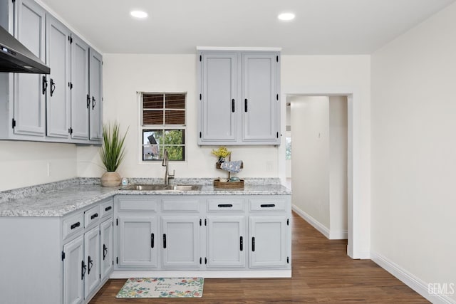 kitchen featuring recessed lighting, a sink, baseboards, wall chimney range hood, and dark wood finished floors