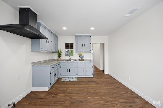 kitchen with dark wood-style flooring, visible vents, a sink, wall chimney range hood, and baseboards