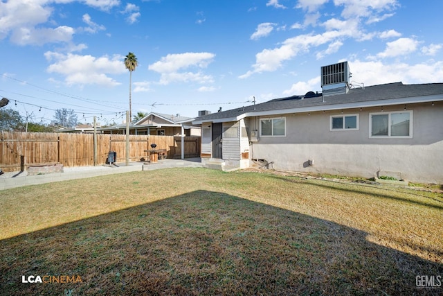 rear view of house with central AC unit and a yard