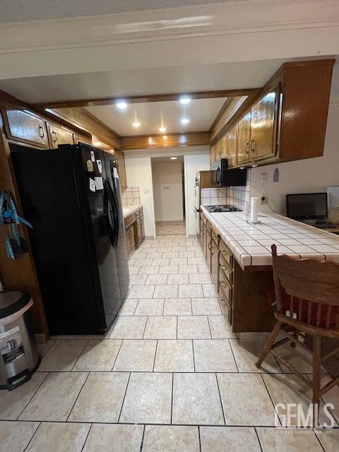 kitchen with decorative backsplash, a tray ceiling, black appliances, light tile patterned floors, and tile counters