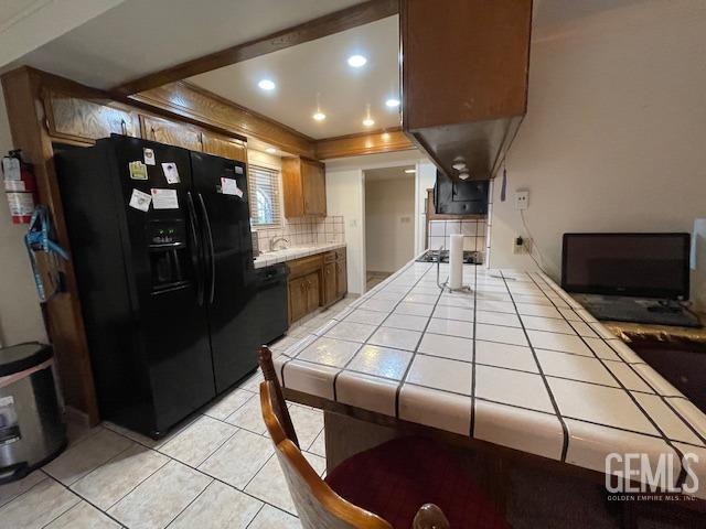 kitchen featuring tile counters, black fridge with ice dispenser, light tile patterned floors, and backsplash