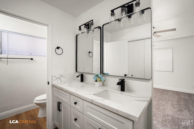 bathroom featuring double vanity, toilet, baseboards, and a sink