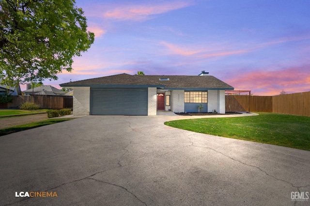 ranch-style home with brick siding, fence, a front yard, driveway, and an attached garage