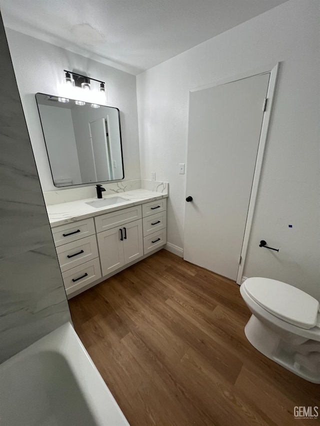 full bath with toilet, a tub to relax in, wood finished floors, and vanity