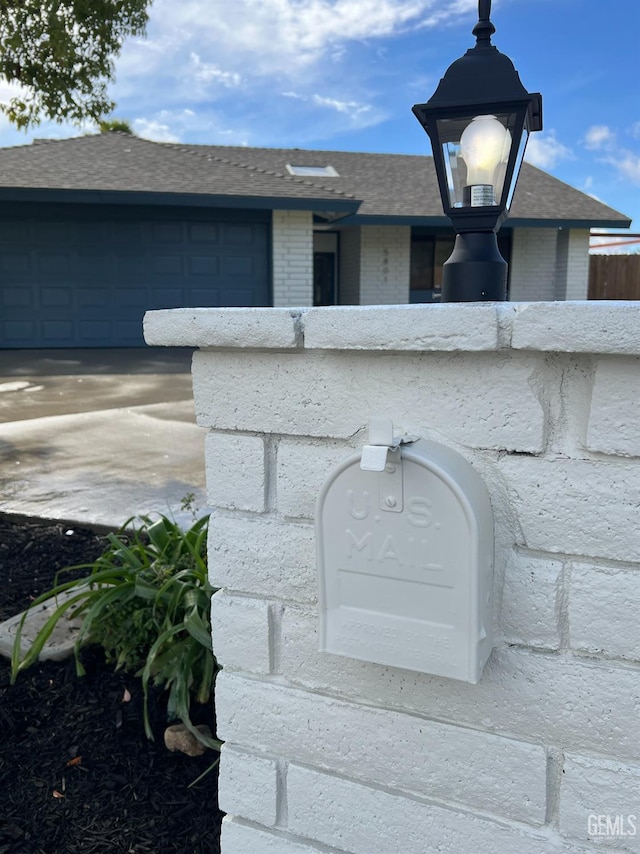 exterior details featuring brick siding, a shingled roof, concrete driveway, and fence