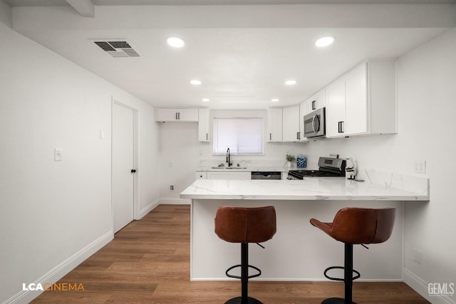 kitchen featuring light stone countertops, visible vents, a peninsula, a sink, and stainless steel appliances