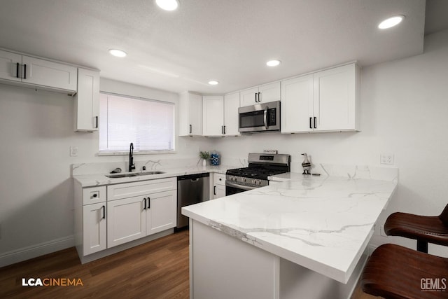 kitchen with a sink, white cabinetry, stainless steel appliances, a peninsula, and light stone countertops