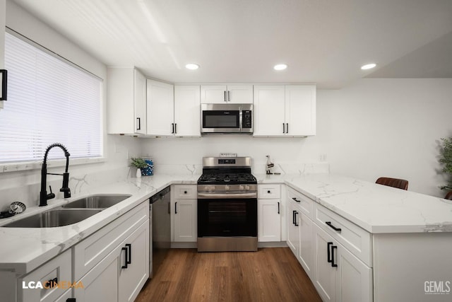 kitchen with appliances with stainless steel finishes, white cabinetry, a peninsula, and a sink