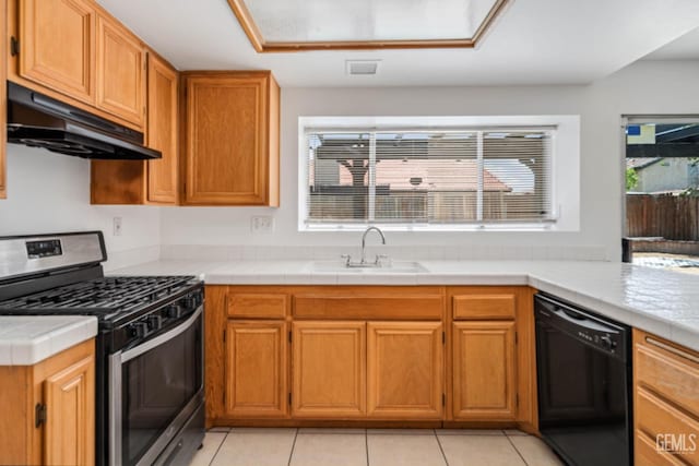 kitchen featuring stainless steel gas stove, black dishwasher, under cabinet range hood, a sink, and light tile patterned floors