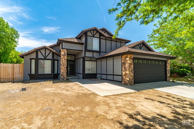 english style home featuring a tiled roof, fence, an attached garage, stone siding, and stucco siding