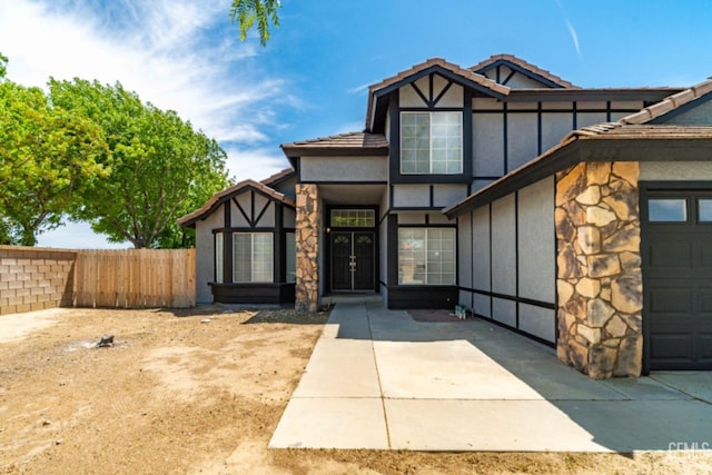 view of front of property featuring a tiled roof, board and batten siding, fence, stone siding, and stucco siding