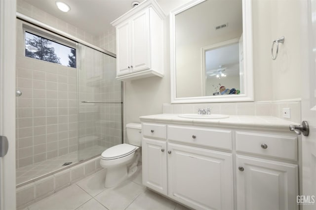 bathroom with tile patterned flooring, toilet, vanity, visible vents, and a tile shower