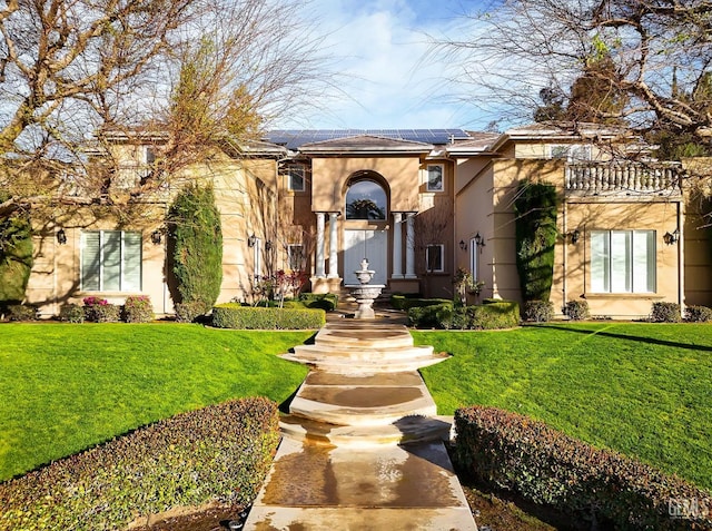 mediterranean / spanish house featuring solar panels, a front yard, and stucco siding