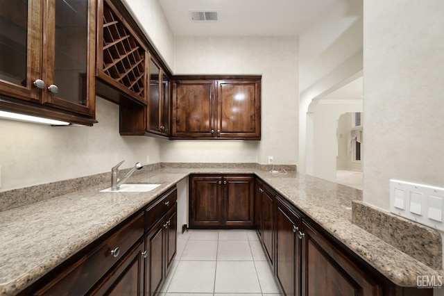 kitchen with light stone counters, light tile patterned floors, visible vents, a sink, and dark brown cabinets