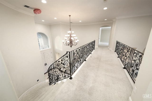 hallway featuring visible vents, an inviting chandelier, ornamental molding, carpet flooring, and an upstairs landing