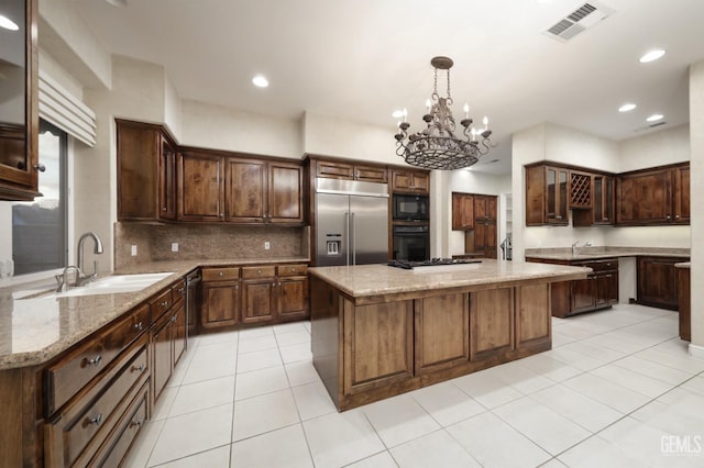 kitchen featuring a center island, visible vents, a sink, light stone countertops, and black appliances