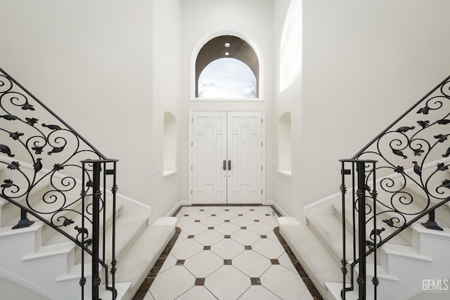 foyer with stairs, light floors, a towering ceiling, and baseboards