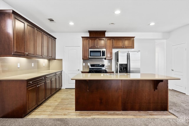 kitchen with sink, a breakfast bar area, a center island with sink, appliances with stainless steel finishes, and light wood-type flooring