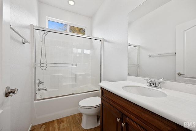 full bathroom featuring hardwood / wood-style floors, vanity, bath / shower combo with glass door, and toilet