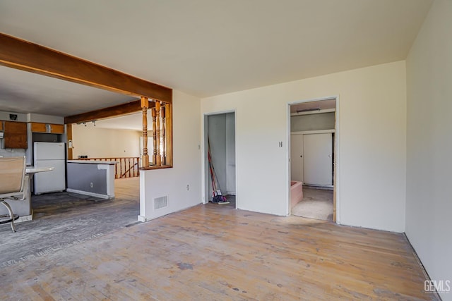 unfurnished living room with beamed ceiling and light wood-type flooring