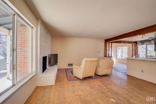 living room with a fireplace, beam ceiling, and light hardwood / wood-style flooring