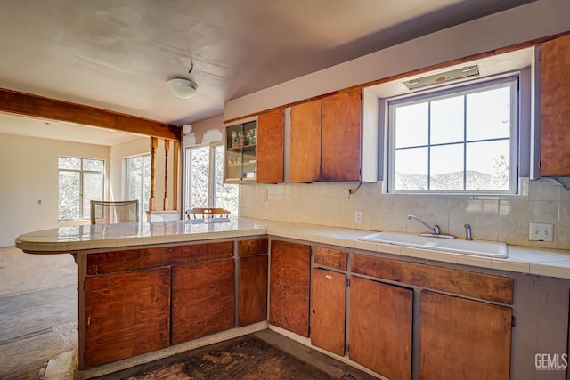 kitchen with sink, decorative backsplash, tile counters, and kitchen peninsula