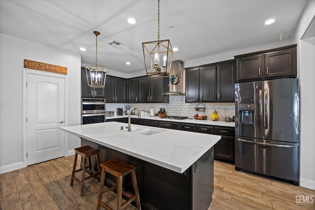 kitchen featuring a sink, a breakfast bar, an inviting chandelier, light wood-style flooring, and appliances with stainless steel finishes