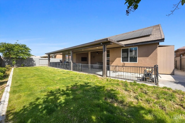 back of house featuring a patio, a fenced backyard, a yard, and solar panels