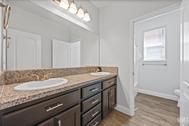 bathroom featuring double vanity, toilet, wood finished floors, and a sink